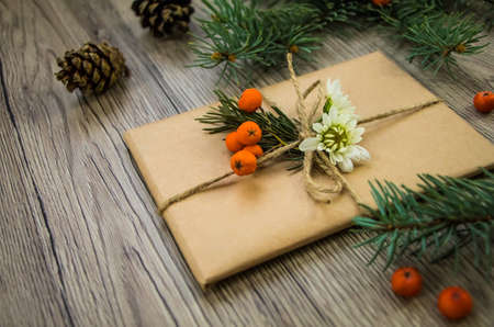 Christmas present wrapped in kraft paper with natural decoration, berries, cones and flowers. Rustic wooden background from above. Angle viewの写真素材