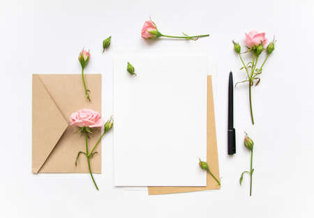 Flat lay shot of letter and eco paper envelope on white background. Wedding invitation cards or love letter with pink roses. Valentine's day or other holiday concept, top view, flat lay, overhead viewの写真素材