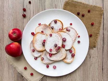 Home made pancakes with cranberries and sugar powder on a white plate. Wooden table, rustic decoration, apples and berries. Top view, flat lay, view from aboveの写真素材
