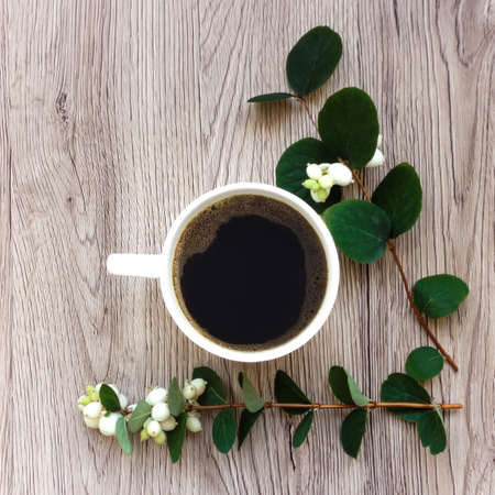 Cup of black coffee decorated with green branches of ghostberry on wooden table. Top view, flat lay,...