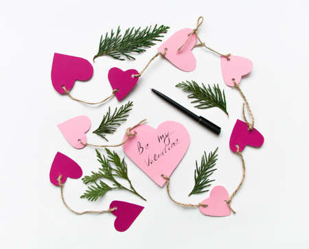 Bright pink paper hearts connected with a rope. Cards for Valentine's day, decorated with thuja branches, Be My Valentine handwritten text. Flat lay on white background, top viewの写真素材