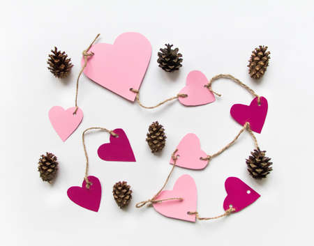 Bright pink paper hearts connected with a rope. Cards for Valentine's day, decorated with cones. Flat lay on white background with place for text, top viewの写真素材