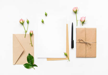 Letter, envelope and a present in eco paper on white background. Wedding invitation cards or love letter with pink roses. Valentine's day or other holiday concept, top view, flat lay, overhead viewの写真素材