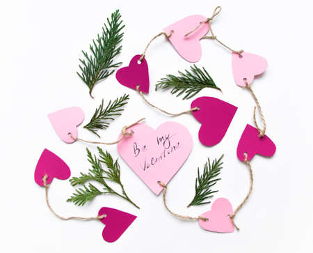 Bright pink paper hearts connected with a rope. Cards for Valentine's day, decorated with thuja branches, Be My Valentine handwritten text. Flat lay on white background, top viewの写真素材