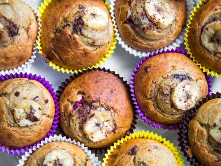 Homemade organic banana muffins in bright paper decorated with banana slice and chocolate crumb. Fresh cupcakes baked at home, tasty and beautiful. Top view, flat layの写真素材