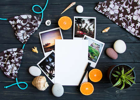Holiday resort elements: photos, stones, seashells, citrus fruits on black vintage wooden background. Blank page, travel photo, tropic vacation memories. Flat lay, top viewの写真素材