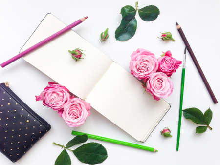 Colorful composition with sketchbook, roses, watercolors and pencils. Flat lay on white table, top viewの写真素材