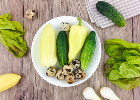 Colorful composition with vegetables and quail eggs on a plate on wooden background. Vegetarian concept, eco products for salad. Easter background. Flat lay, top view with copy spaceの写真素材