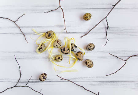 Easter festive background, few quail eggs decorated with yellow raffia ribbon on a white vintage wooden table. Flat lay, top view, minimal conceptの写真素材