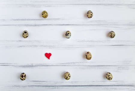 Decorative light pattern with quail eggs and a heart on white wooden vintage table. Flat lay, top view, natural still life, eggs polka dotの写真素材