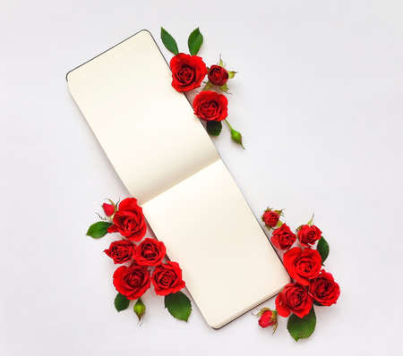 Colorful composition with sketchbook and red roses. Flat lay on white table, top view, copy space