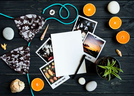 Holiday resort elements: photos, stones, seashells, citrus fruits on black vintage wooden background. Blank page, travel photo, tropic vacation memories. Flat lay, top viewの写真素材