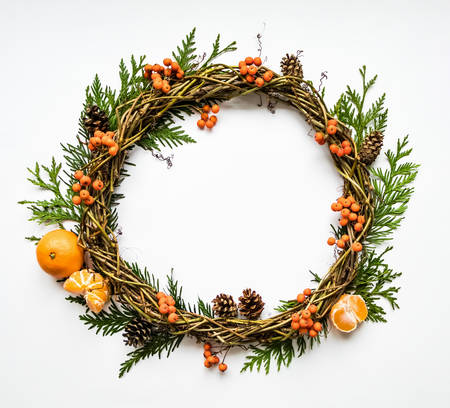 Festive wreath of grape vines with tangerines, thuja branches, rowanberries and cones. Christmas DIY wreath. New Year round wreath on white background. Flat lay, top viewの写真素材