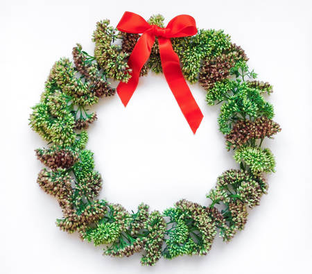 Green floral round wreath frame with a red ribbon on white background. Flat lay, top view, view from above. Autumn or winter decorationの写真素材