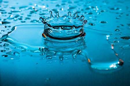 Dynamic blue water splash surrounded by a myriad of droplets falling on the surface of the liquidの写真素材
