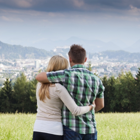 Rear view of a young vacation couple embracing while looking and standing outdoorsの写真素材