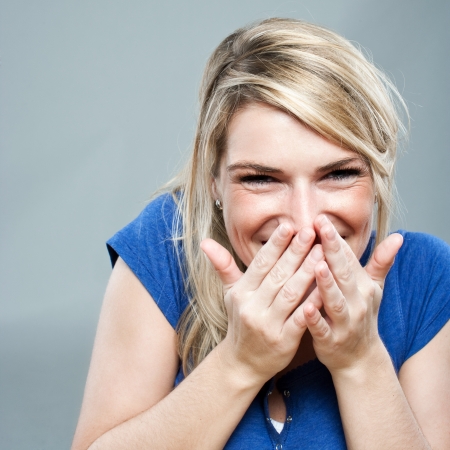 Portrait of a beautiful and shy blond woman giggling and hiding her smile with the handsの写真素材