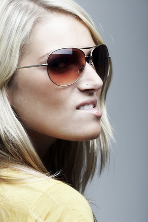 Closeup portrait of a beautiful blond woman with sunglasses looking over her shoulder and biting her lower lipの写真素材