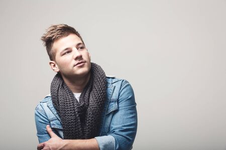Fashion portrait of a young man crossing arms and looking away on a gray backgroundの写真素材