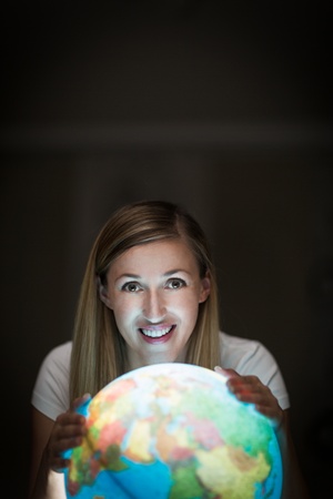 Pretty young blond woman smiling while using a lit earth globe in the dark showing East Africa, the Middle East and Asiaの写真素材