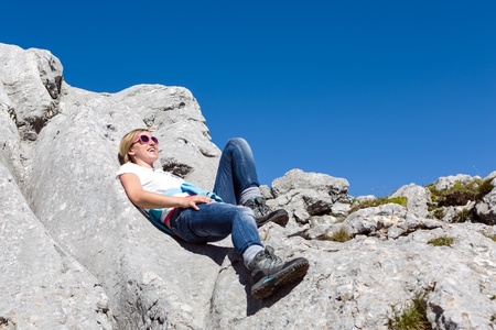 Pretty young woman resting during the hike laying on large boulders and enjoying the sun on a bright dayの写真素材