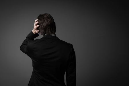 Studio shot of a male model expressing bad times by facing the wall and one hand on his head, isolated on gray.の写真素材