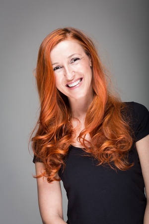 Friendly warmhearted woman with a lovely smile and gorgeous wavy red hair, studio portrait on greyの写真素材