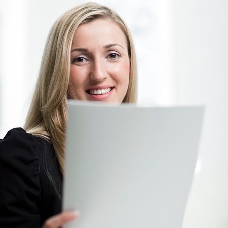 Portrait of a smiling businesswoman with a document in her hand looking at the camera with closeup focus to her faceの写真素材