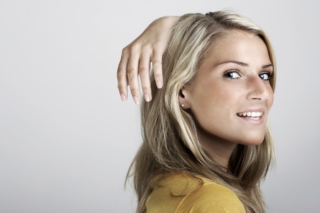 Beauty fashion portrait of a young blond woman smiling and holding the hand high behind the headの写真素材