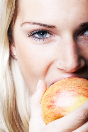 Close-up portrait of a beautiful blonde woman with blue eyes bitting an appleの写真素材