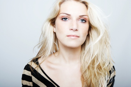High-key beauty portrait of a caucasian blonde woman with blue eyes, looking at camera with a serious expression, on a gray backgroundの写真素材