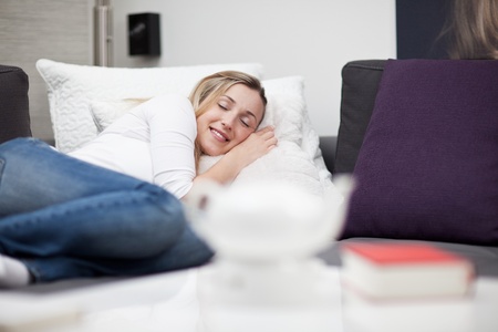 Beautiful young woman sleeping in bed taking a midday nap curled up on top of the bed with a serene smile on her face as she enjoys her dreamsの写真素材