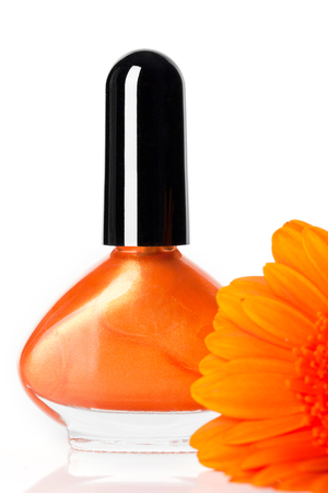 Modern trendy orange nail varnish in a stylish globular bottle with a fresh Gerbera daisy in the foreground over whiteの写真素材