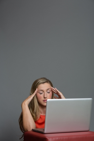 Very tired young woman working on a laptop with an headache and massaging head with closed eyesの写真素材