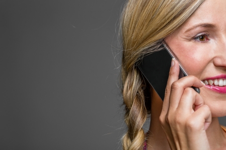 Close-up portrait of a blond woman talking on the mobile phone with copy-space and gray backgroundの写真素材