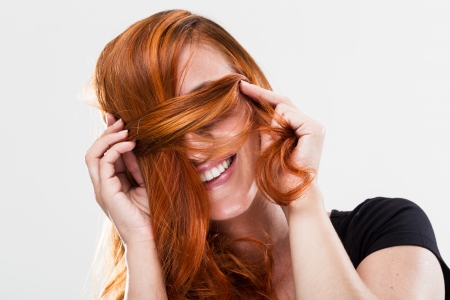 Playful and happy young redhead woman smiling and being shy covering her eyes with the hairの写真素材