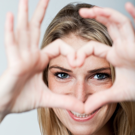 Romantic woman making a heart gesture with her hands framing her laughing eyes as she shows her feelings of love and affectionの写真素材
