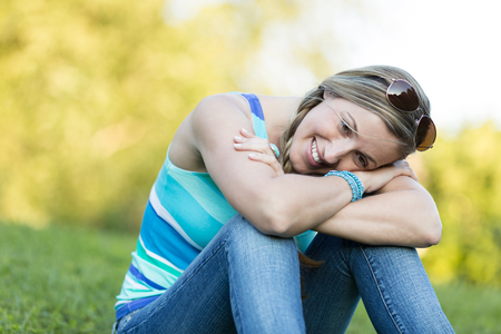 Young woman sitting on the grass with her head resting on her arms thinking while enjoying the peace and tranquillity of natureの写真素材