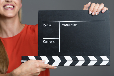 Smiling woman holding a clapperboard during a film production to give the sound to commence recording of the audio during each new takeの写真素材
