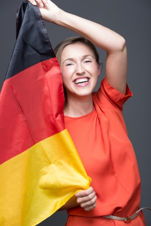 Enthusiastic patriotic woman with the German flag laughing vivaciously as she waves it in the air with her handsの写真素材
