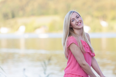 Attractive young woman with long blond hair standing in a pretty stylish pink top enjoying autumn outdoors with copyspaceの写真素材