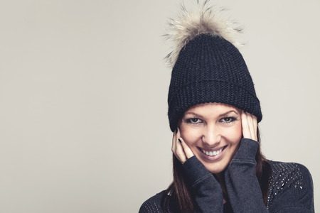 Friendly smiling young woman in winter fashion wearing a black knitted beanie with a fun furry...