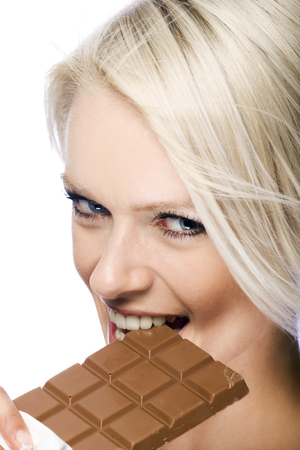 Sensual image of a beautiful young woman biting a bar of milky chocolate gripping it between the teeth as she looks teasingly at the camera, on whiteの写真素材