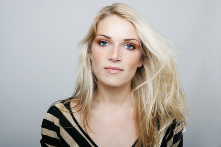Beautiful blond woman with a sincere gentle expression full of empathy looking directly at the camera, studio head and shoulders on greyの写真素材