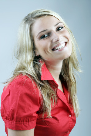 Happy beautiful young woman with long blond hair wearing a red blouse laughing at the cameraの写真素材