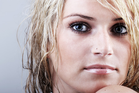 Beautiful blond woman with tousled damp hair and a sombre enigmatic gaze staring intently at the camera, close up view of her faceの写真素材