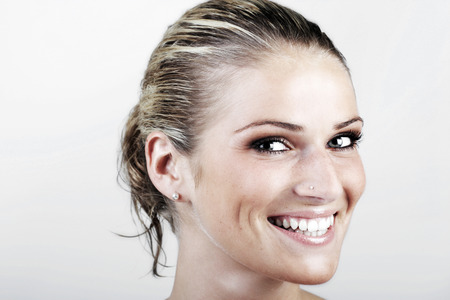 Beautiful vivacious blond woman with wet hair looking at the camera with a beaming smile, close up face portrait on whiteの写真素材
