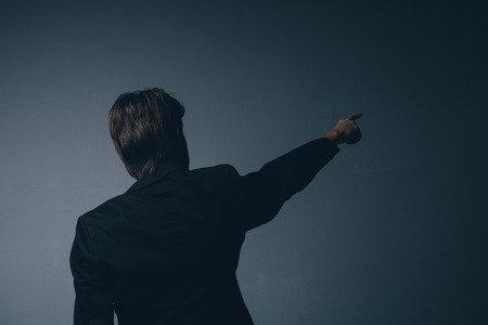 Businessman in a stylish suit standing with his back to the camera pointing ahead and calling your...