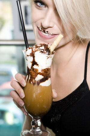 Close up view of a beautiful woman drinking a large glass of iced coffee with enjoyment and smiling at the camera with a moustache of cream and chocolateの写真素材