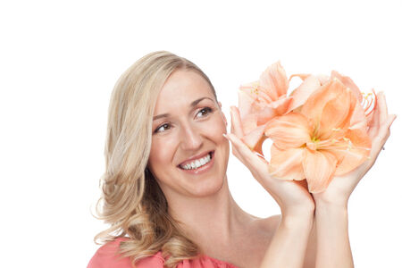 Attractive woman with a lovely happy smile holding up beautiful apricot colored Amaryllis flowers in the palms of her hands, isolated on whiteの写真素材